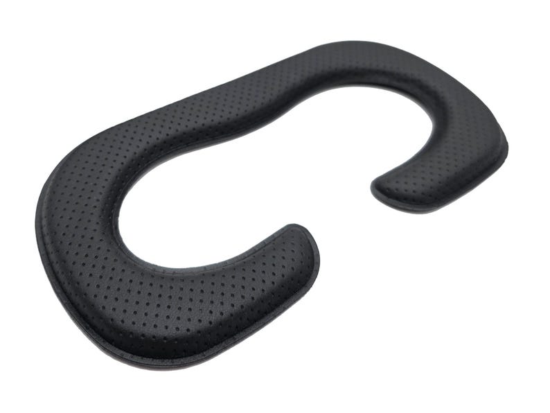May include: Black, curved VR headset facial interface replacement. The pad is made of a soft, perforated material for comfort. The shape is designed to fit around the eyes and nose, with a curved design for the forehead and cheeks.