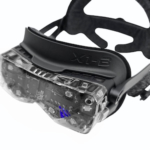 May include: A black VR headset with the text "X1-3" on the top. The headset has a clear plastic visor revealing internal components. The design includes a head strap and a cushioned support for the forehead.