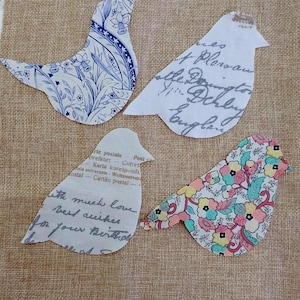 Peut inclure: Quatre découpes d'oiseaux en tissu avec différents motifs. L'un présente un motif floral bleu et blanc, un autre un motif floral avec des fleurs roses, jaunes et bleues. Les deux autres oiseaux ont du texte imprimé.