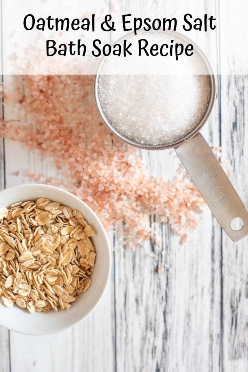 May include: A white bowl filled with rolled oats, a measuring cup filled with Epsom salt, and pink Himalayan salt scattered on a white wooden surface. The text "Oatmeal & Epsom Salt Bath Soak Recipe" is at the top of the image.