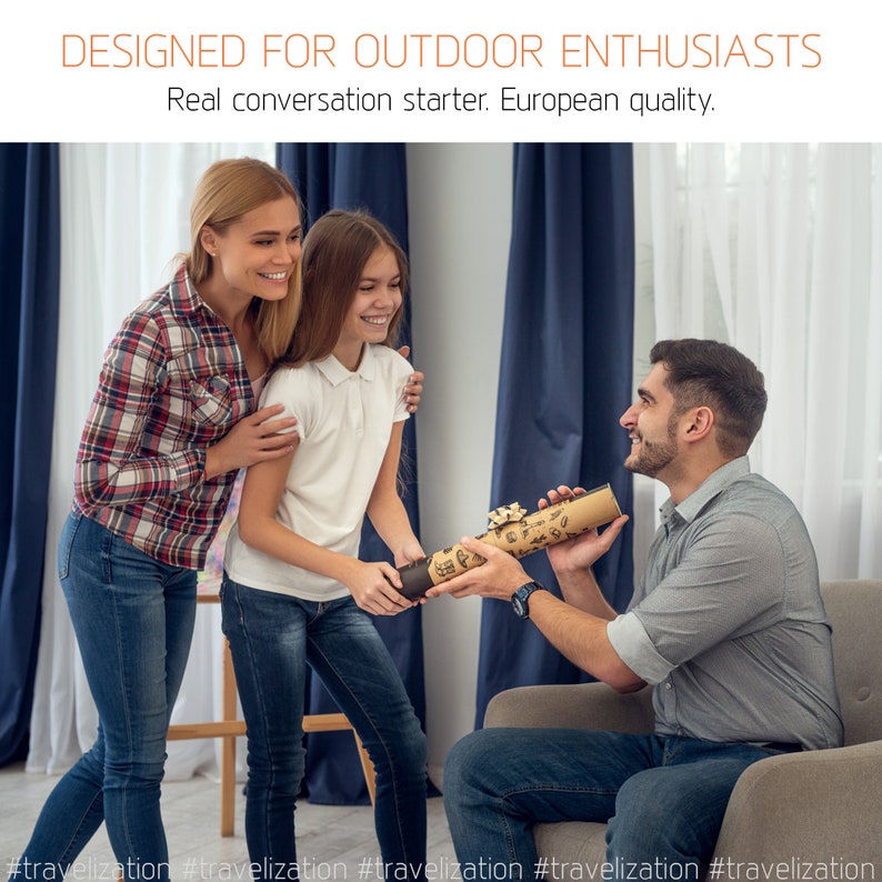 May include: A family of three, a man, a woman, and a young girl, are gathered together in a living room. The man is holding a rolled-up map or poster, while the woman and girl are smiling at him. The text on the poster reads "DESIGNED FOR OUTDOOR ENTHUSIASTS Real conversation starter. European quality."