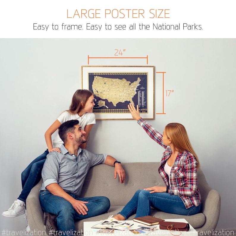 May include: A family of three are looking at a gold foil map of the United States in a black frame. The map is 24 inches wide and 17 inches tall. The map is hanging on a white wall. The family are sitting on a grey sofa. The map is a scratch-off map where you can scratch off the gold foil to reveal the map underneath.