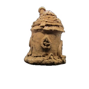 May include: A small, brown, clay-like fairy house with a thatched roof and a small window. The house is sitting on a base that looks like dirt.
