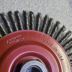 May include: A red Osborn wire brush with a silver center nut. The brush has tightly packed, twisted steel wires. The words "MADE IN USA" are visible on the red metal housing.