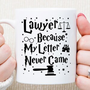 May include: White ceramic mug with a black design that reads "Lawyer Because My Letter Never Came". The design includes a scale of justice, glasses, a lightning bolt, a castle, and a gavel.
