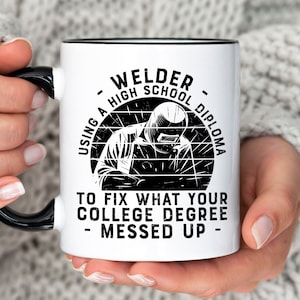 May include: White ceramic mug with a black rim and handle. The mug features a black and white illustration of a welder with the text "Welder - Using a High School Diploma to fix what your college degree messed up - "