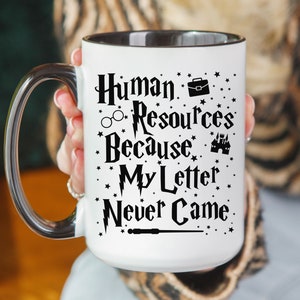 May include: White mug with a black rim and handle. The mug has a black graphic that says "Human Resources Because My Letter Never Came" with a Hogwarts castle, glasses, and a briefcase.