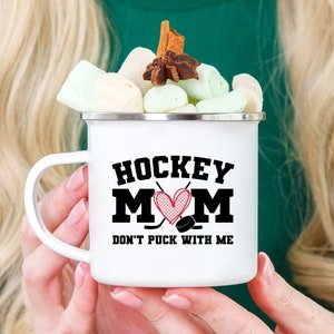 May include: White enamel mug with a black and red graphic that says "Hockey Mom Don't Puck With Me".