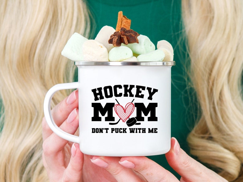 May include: White enamel mug with a black and red graphic that says "Hockey Mom Don't Puck With Me".