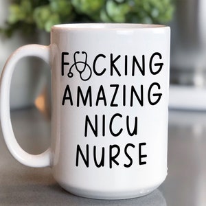Op de afbeelding: Witte keramische koffiemok met een zwarte afbeelding waarop "F*CKING AMAZING NICU NURSE" staat met een stethoscoopicoon.