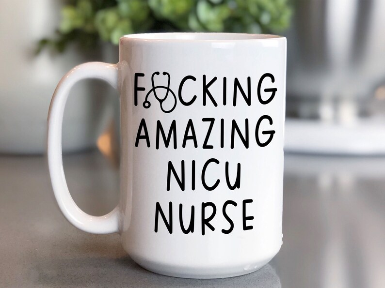 Op de afbeelding: Witte keramische koffiemok met een zwarte afbeelding waarop "F*CKING AMAZING NICU NURSE" staat met een stethoscoopicoon.