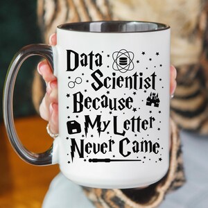 May include: White ceramic mug with a black rim and handle. The mug has a black design that says "Data Scientist Because My Letter Never Came" with various symbols including a pair of glasses, a database symbol, a castle, and a wand.