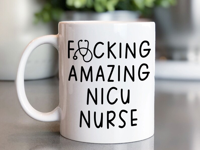 Op de afbeelding: Witte keramische koffiemok met een zwart ontwerp met de tekst "F*CKING AMAZING NICU NURSE" met een stethoscoop afbeelding.