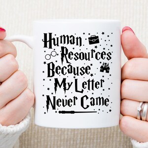 May include: White ceramic mug with a black design that says "Human Resources Because My Letter Never Came". The design includes a briefcase, glasses, a castle, and a wand.