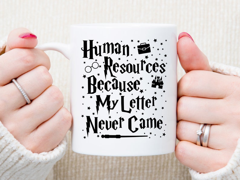 May include: White ceramic mug with a black design that says "Human Resources Because My Letter Never Came". The design includes a briefcase, glasses, a castle, and a wand.