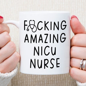 Op de afbeelding: Witte keramische mok met zwarte tekst die "F*CKING AMAZING NICU NURSE" zegt met een stethoscoopicoon.