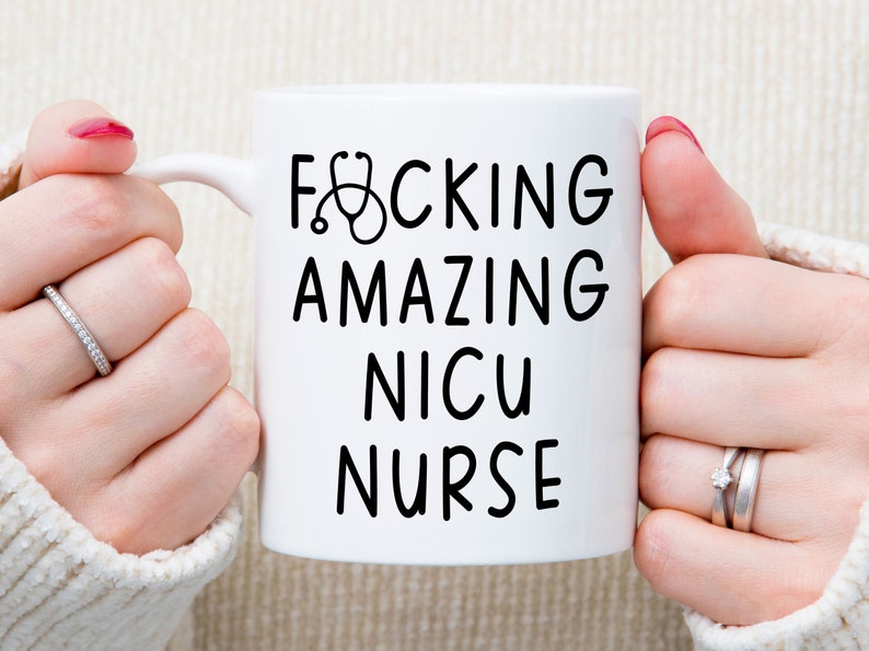 Op de afbeelding: Witte keramische mok met zwarte tekst die "F*CKING AMAZING NICU NURSE" zegt met een stethoscoopicoon.