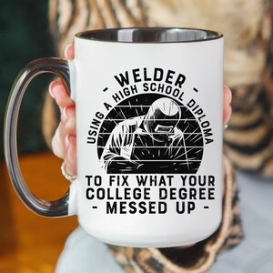 May include: White ceramic mug with a black interior and handle. The mug features a black and white illustration of a welder with the text "Welder - Using a High School Diploma to Fix What Your College Degree Messed Up - "