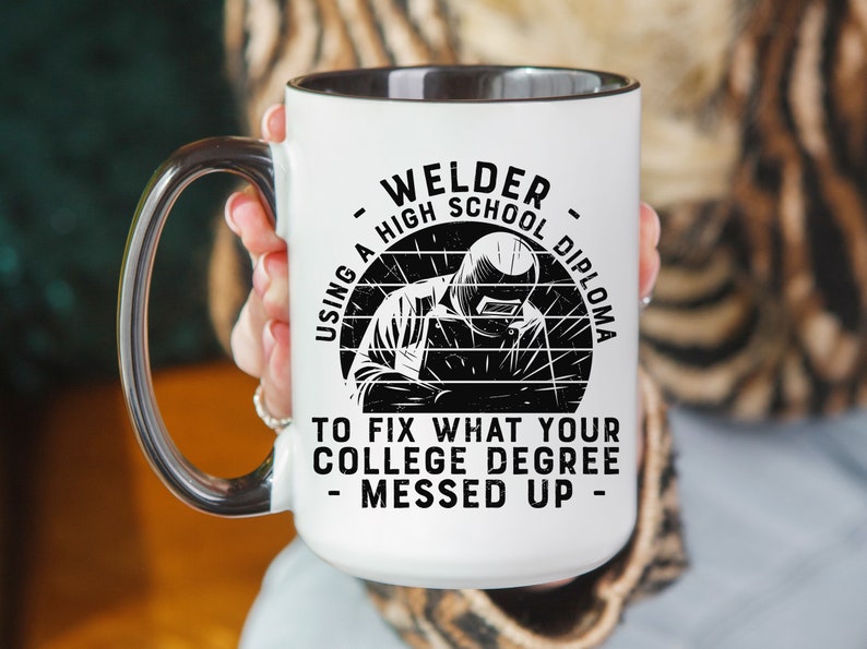 May include: White ceramic mug with a black interior and handle. The mug features a black and white illustration of a welder with the text "Welder - Using a High School Diploma to Fix What Your College Degree Messed Up - "