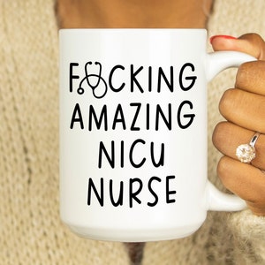 Op de afbeelding: Witte keramische koffiemok met zwarte tekst die "F*CKING AMAZING NICU NURSE" luidt met een stethoscoopicoon boven het woord "F*CKING".