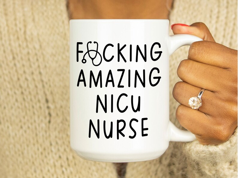 Op de afbeelding: Witte keramische koffiemok met zwarte tekst die "F*CKING AMAZING NICU NURSE" luidt met een stethoscoopicoon boven het woord "F*CKING".