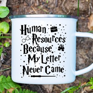 May include: White enamel mug with a black graphic that reads "Human Resources Because My Letter Never Came." The graphic includes a briefcase, glasses, a lightning bolt, a castle, and a wand.