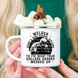 May include: White enamel camping mug with a black graphic that reads "Welder - Using a High School Diploma to Fix What Your College Degree Messed Up - ". The graphic features a welder with a welding mask on.