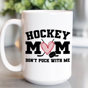 May include: White ceramic coffee mug with a black and red design. The mug features the text "HOCKEY MOM DON'T PUCK WITH ME" with a heart and hockey sticks.