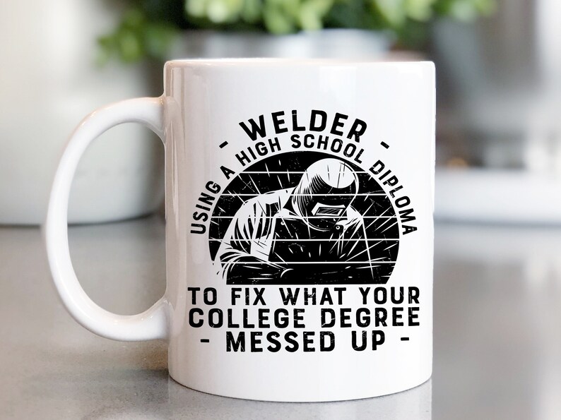 May include: White ceramic coffee mug with a black graphic of a welder wearing a welding mask and the text "Welder - Using a High School Diploma to fix what your college degree messed up - "