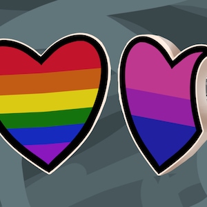 Puede incluir: Dos pines en forma de corazón con rayas de arcoíris. El pin de la izquierda es un arcoíris tradicional con rayas rojas, naranjas, amarillas, verdes, azules, índigo y violetas. El pin de la derecha es una bandera del orgullo bisexual con rayas rosas, moradas y azules.