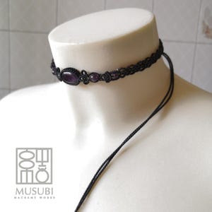 Op de afbeelding: Een zwarte macramé choker ketting met een paarse edelsteen hanger. De ketting is verstelbaar en heeft een eenvoudig ontwerp.