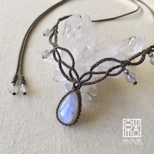 May include: A handmade macrame necklace with a pear-shaped, iridescent moonstone pendant. The necklace has a dark brown cord with intricate knotting and small, round beads. The design includes a sliding knot closure for adjustable length.