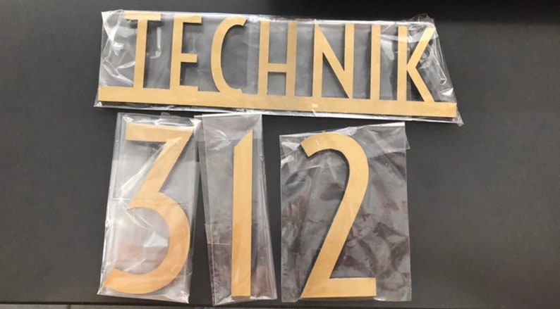 May include: Gold-colored wooden letters spelling "TECHNIK" and the numbers "312" on a white background.