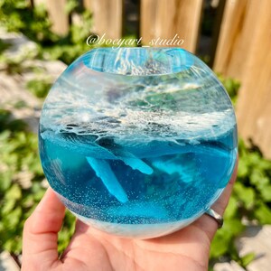 Könnte beinhalten: Eine klare Glaskugel mit einer blauen und weißen Ozeanszene aus Harz. Die Szene zeigt weiße Wellen, blaues Wasser und eine weiße Walflosse.