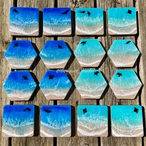 May include: Set of 12 resin coasters featuring a blue and white ocean wave design with a silhouette of a manta ray. The coasters are in a variety of shapes, including square and hexagonal.