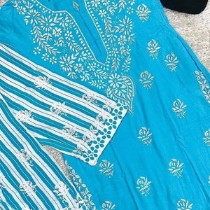 May include: A turquoise blue tunic with white embroidery featuring floral and paisley designs. The tunic has a striped white and turquoise blue sleeve with a white embroidered border.