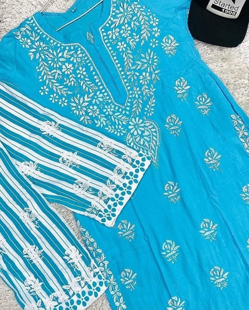 May include: A turquoise blue tunic with white embroidery featuring floral and paisley designs. The tunic has a striped white and turquoise blue sleeve with a white embroidered border.