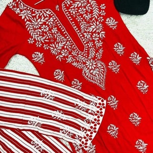 May include: A red and white striped long-sleeve shirt with white embroidery. The shirt has a round neckline and a white embroidered design on the front. The shirt is paired with a red long-sleeve top with white embroidery. The top has a V-neckline and a white embroidered design on the front.