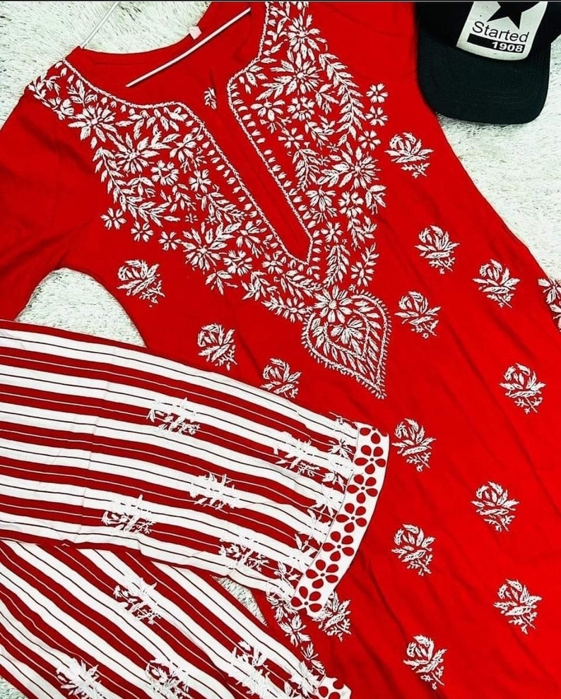 May include: A red and white striped long-sleeve shirt with white embroidery. The shirt has a round neckline and a white embroidered design on the front. The shirt is paired with a red long-sleeve top with white embroidery. The top has a V-neckline and a white embroidered design on the front.