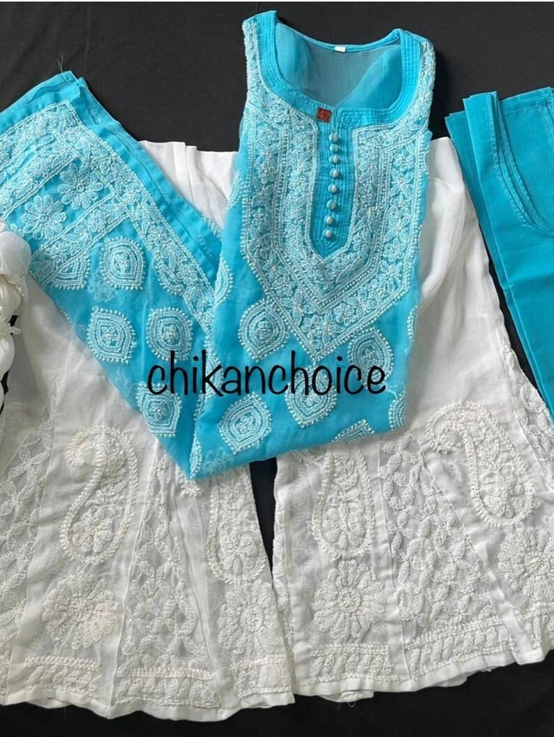 May include: A white and turquoise embroidered dress with a sleeveless top and a long skirt. The dress has a round neckline and a button closure. The skirt is flared and has a scalloped hem. The dress is made of a sheer fabric and is decorated with intricate embroidery.