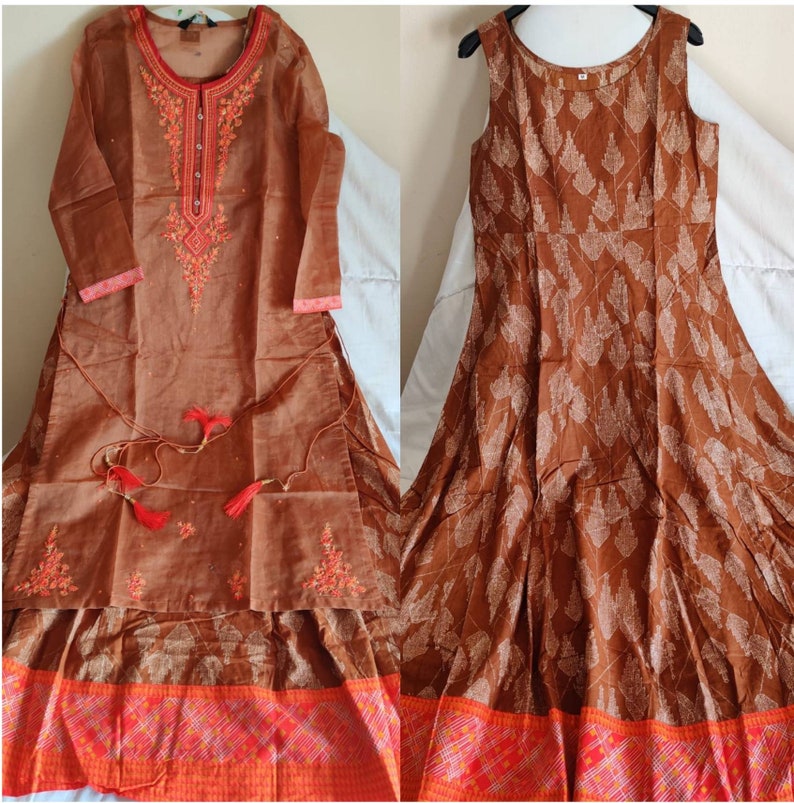 May include: Two brown cotton dresses with embroidered details. The dress on the left has long sleeves and a high neckline. The dress on the right is sleeveless and has a round neckline. Both dresses have a red and orange border at the bottom.