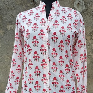 Op de afbeelding: Een wit shirt met lange mouwen en een herhalend bloemenpatroon van kleine rode rozen met groene stengels en bladeren. Het shirt heeft een opstaande kraag, een volledige knoopsluiting aan de voorzijde met doorzichtige knopen en rechte mouwboorden.