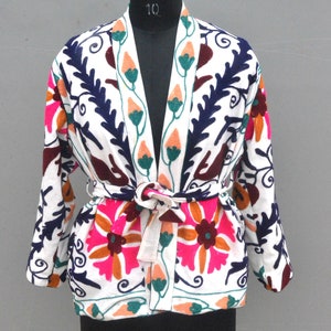 May include: White cotton jacket with a floral embroidery design in pink, orange, green, and blue. The jacket has a tie belt and a V-neck.