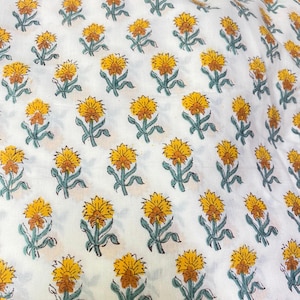 Op de afbeelding: Een witte stof met een herhalend patroon van kleine, gestileerde bloemen met gele bloemblaadjes, oranje harten en gedempte groene stengels en bladeren. De bloemenprint is in een consistent raster over het gehele textieloppervlak geplaatst.