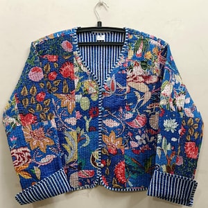 Op de afbeelding: Een blauw gewatteerd jack met een bloemenprint en een gestreepte voering. Het jack heeft een V-hals en een knoopsluiting.