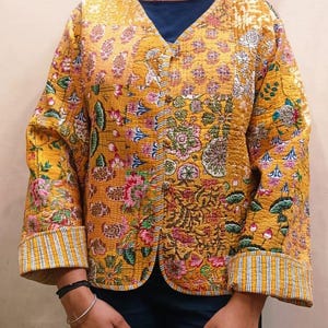 May include: A yellow quilted jacket with a floral print and a button closure. The jacket has long sleeves with striped cuffs.