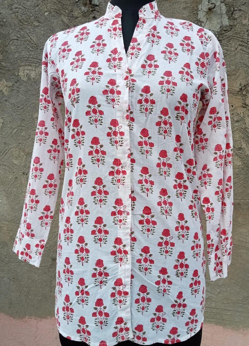 Op de afbeelding: Een wit shirt met lange mouwen en een herhalend bloemenpatroon van kleine rode rozen met groene stengels en bladeren. Het shirt heeft een opstaande kraag, een volledige knoopsluiting aan de voorzijde met doorzichtige knopen en rechte mouwboorden.
