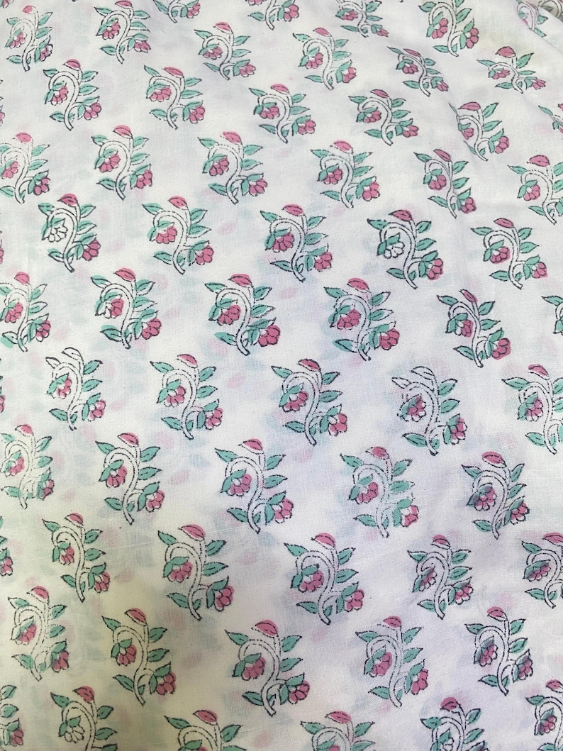 Op de afbeelding: Een witte stof met een herhalend patroon van kleine bloemtakjes. Elk takje bestaat uit groene bladeren en roze bloesems, omlijnd met dunne zwarte lijnen. Het ontwerp is in een consistent rasterpatroon over het textieloppervlak verdeeld.