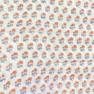 Op de afbeelding: Een witte stof met een herhalend patroon van kleine oranje bloemen met grijsblauwe stengels en bladeren. Het bloemmotief is in een consistent rasterachtig patroon over het gehele oppervlak van het textielmateriaal gerangschikt.