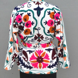 May include: White cotton jacket with colorful floral embroidery. The jacket has a belt and long sleeves.